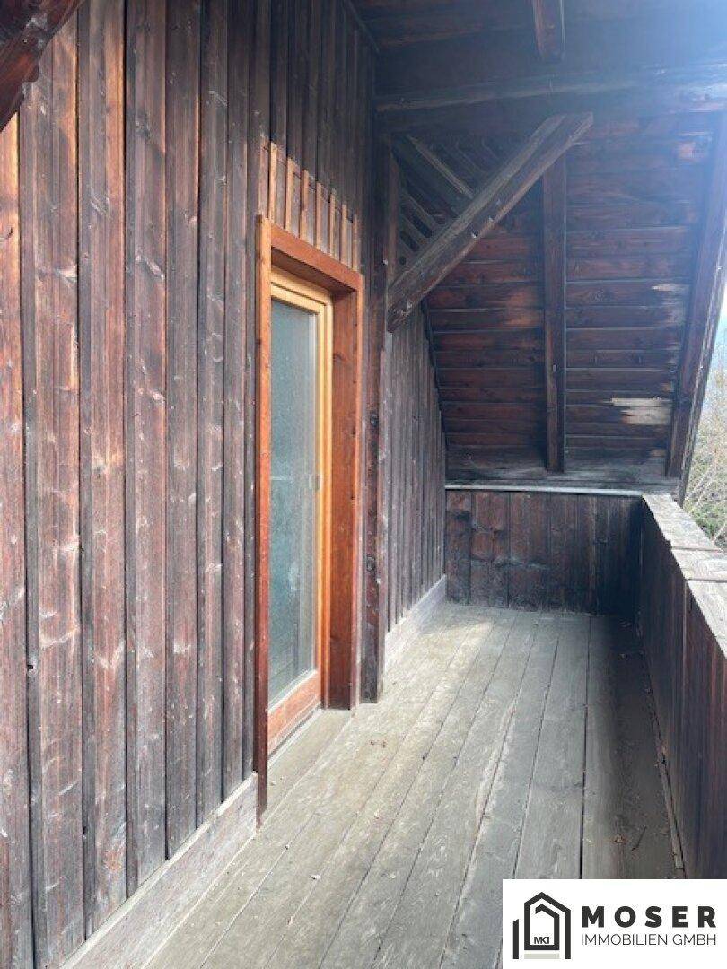 Rustikaler Holzbalkon mit Holzboden und Zugang zu einem Innenraum.