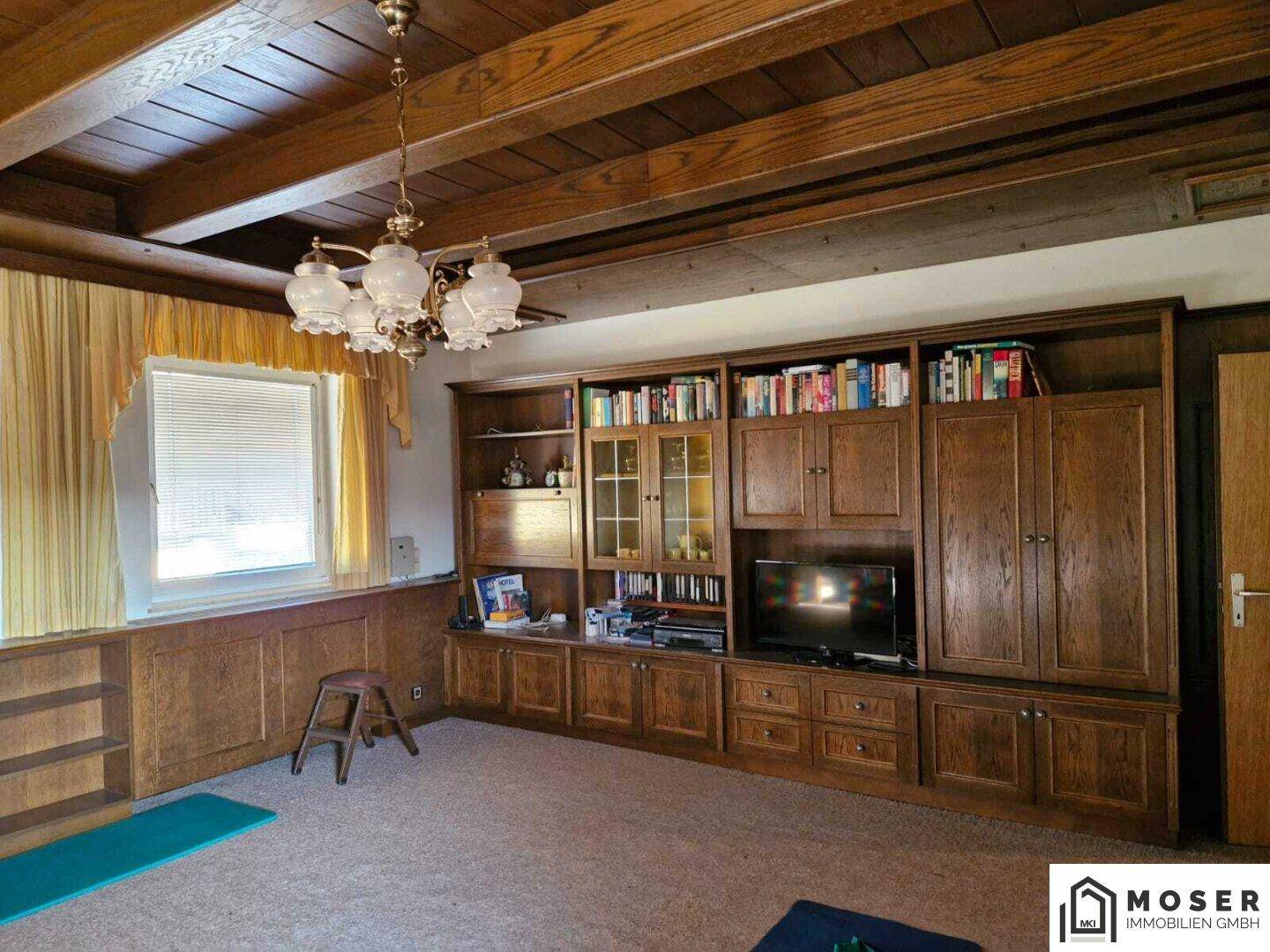 Traditionelles Wohnzimmer mit Holzbalkendecke, Teppichboden und einer großen Schrankwand.