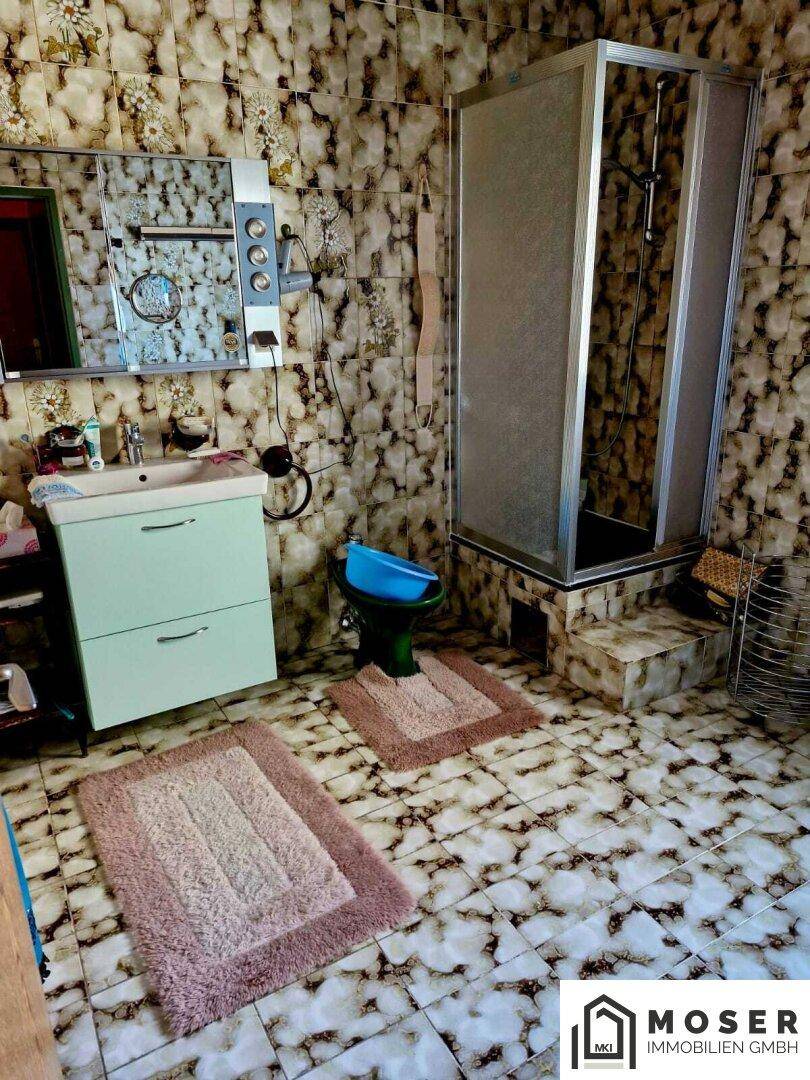 Badezimmer im 80er-Jahre-Stil mit gemusterten Fliesen, Dusche und einem einzelnen Waschbecken.