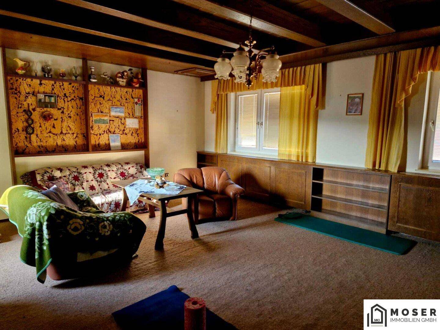 Gemütliches Wohnzimmer mit Holzbalkendecke, Teppichboden und traditionellen Möbeln.