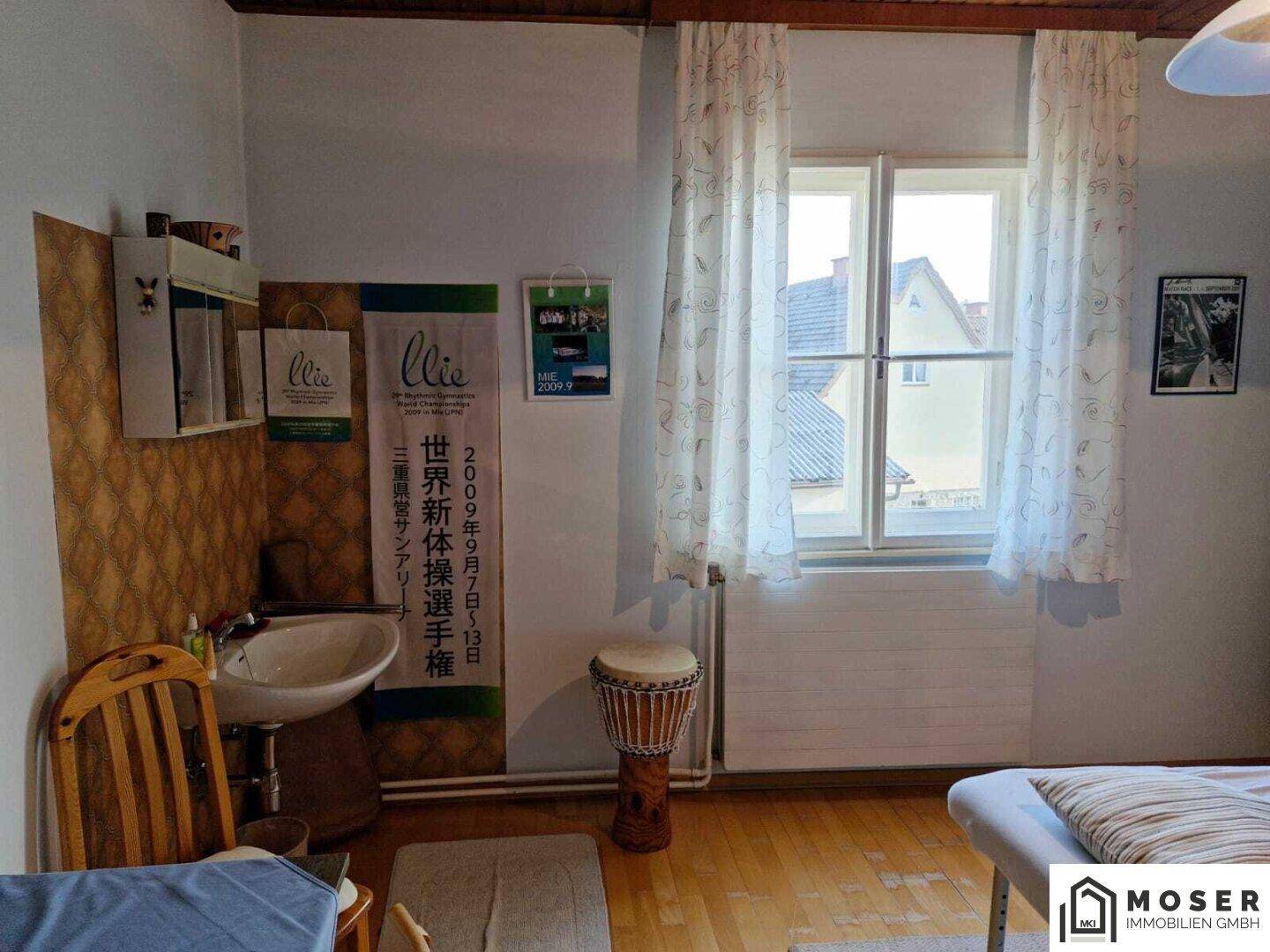Helles Zimmer mit Holzboden, Fenster und einem kleinen Waschbecken, möglicherweise ein Gästezimmer.