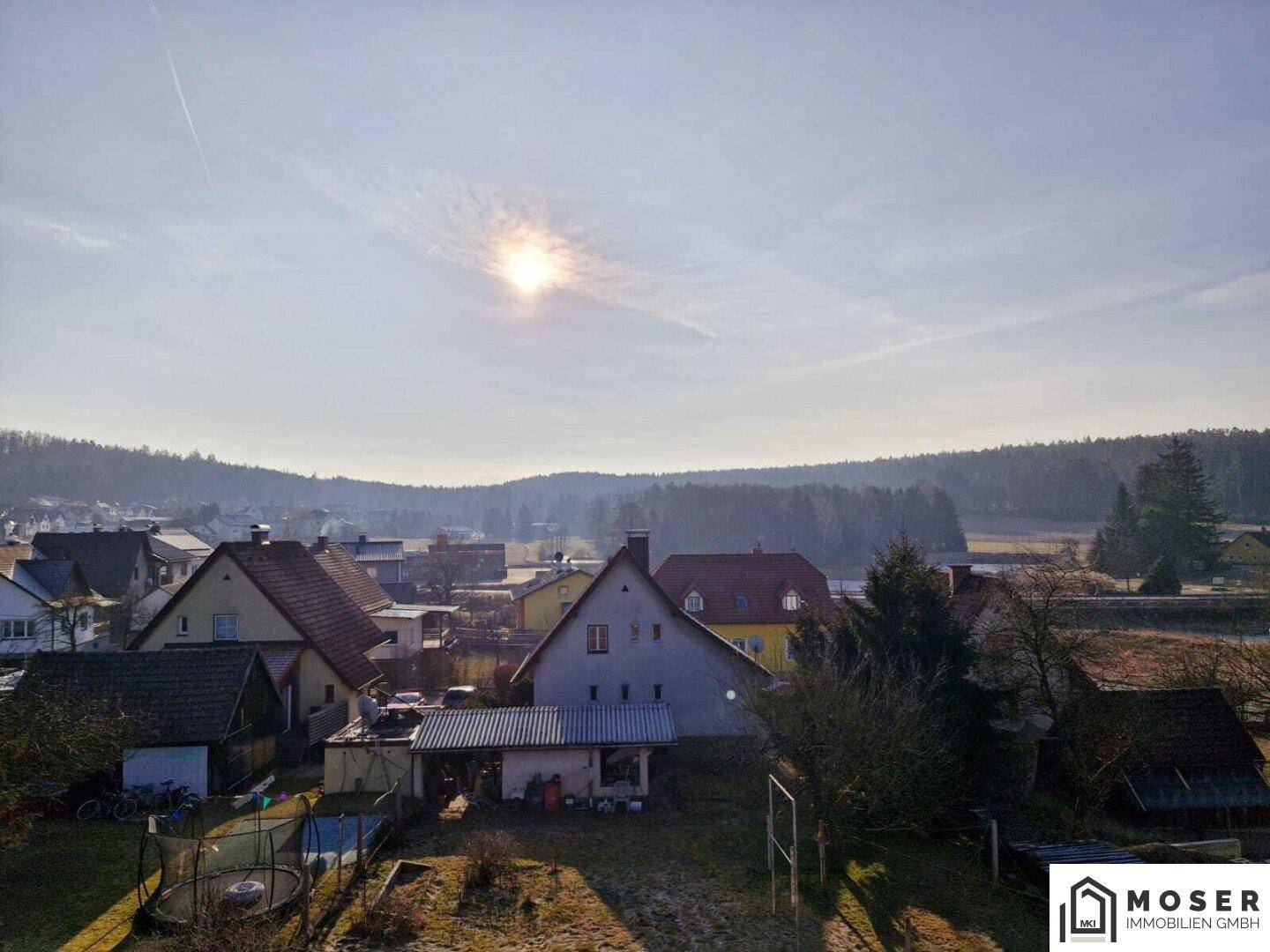 Panoramablick über eine Siedlung in ländlicher Umgebung mit Wald und weitem Himmel.