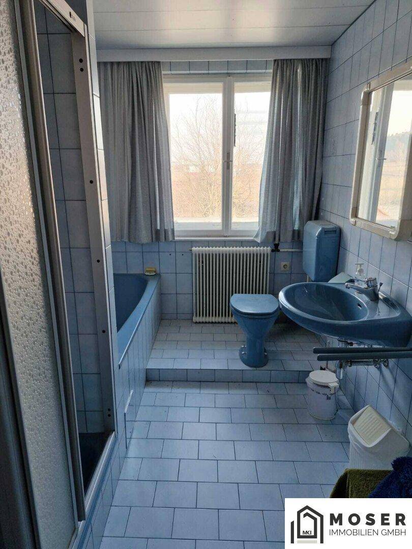 Badezimmer im 80er-Jahre-Stil mit blauen Fliesen, Badewanne und Dusche.