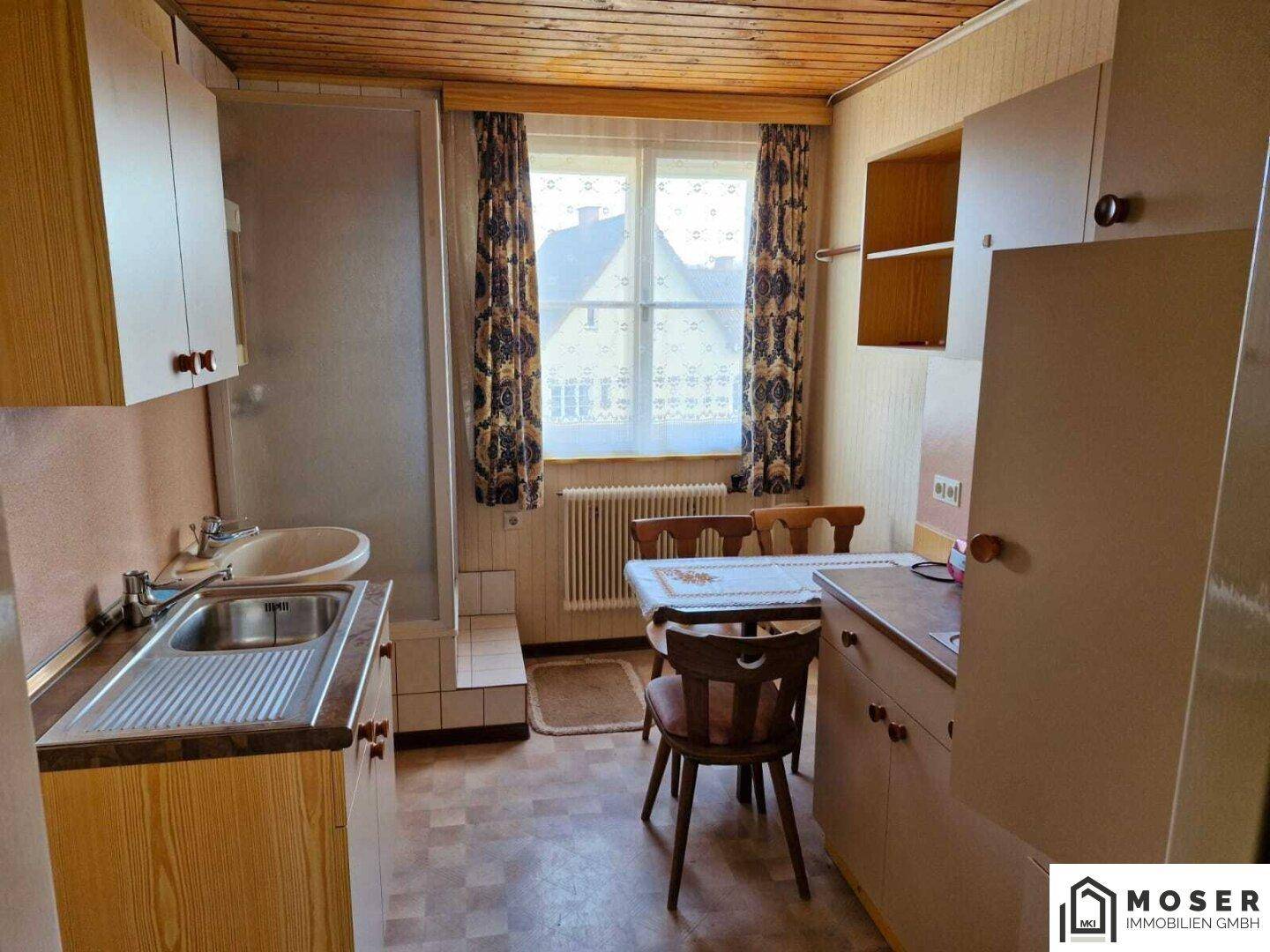 Kleine Küche mit Holzschränken, Spüle, Esstisch und einem Fenster.