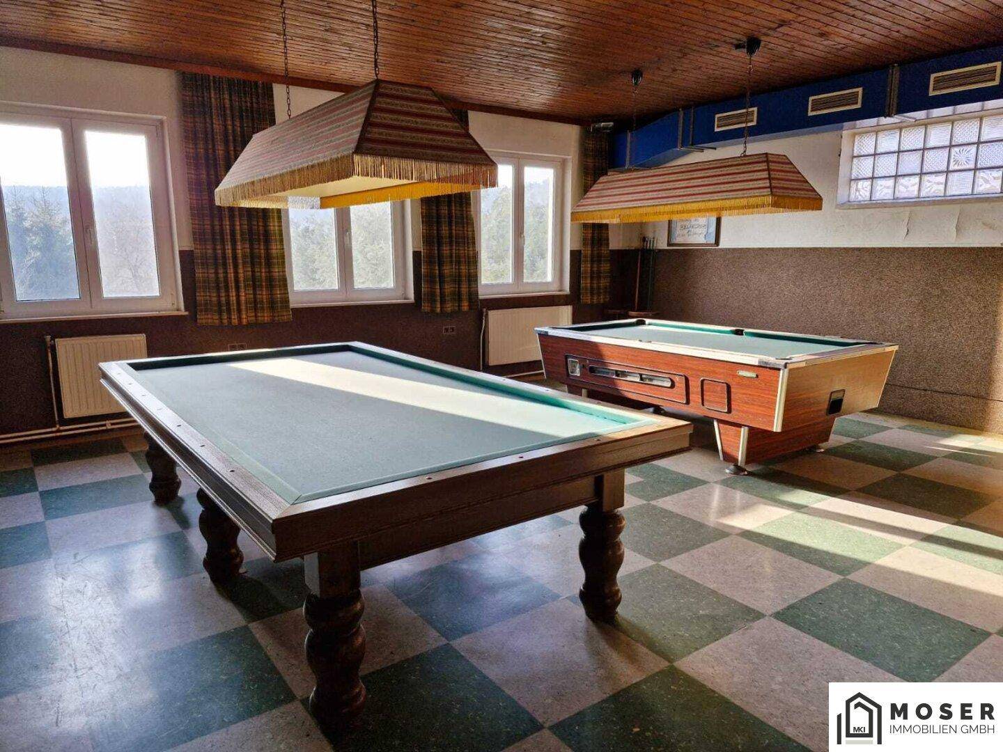 Geräumiger Spielraum mit zwei Billardtischen, kariertem Boden und großen Fenstern.