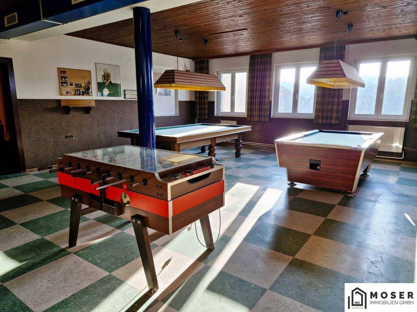 Heller Spielraum mit Billard- und Kickertischen, kariertem Boden und viel Tageslicht.