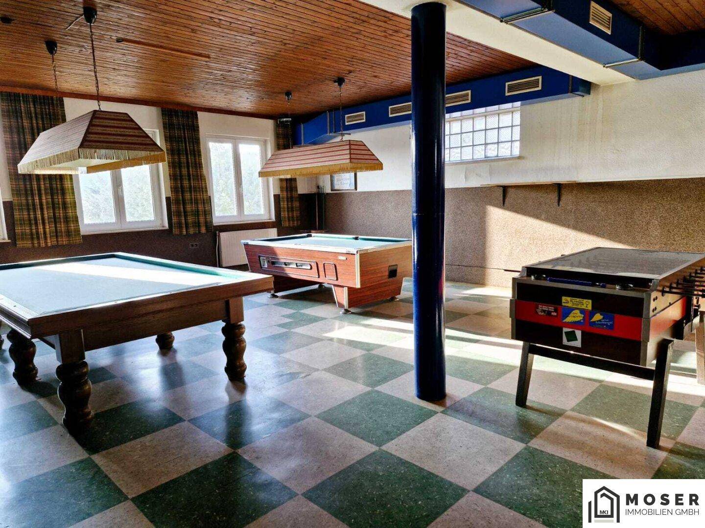 Großer Spielraum mit Billard- und Kickertischen, kariertem Boden und viel natürlichem Licht.