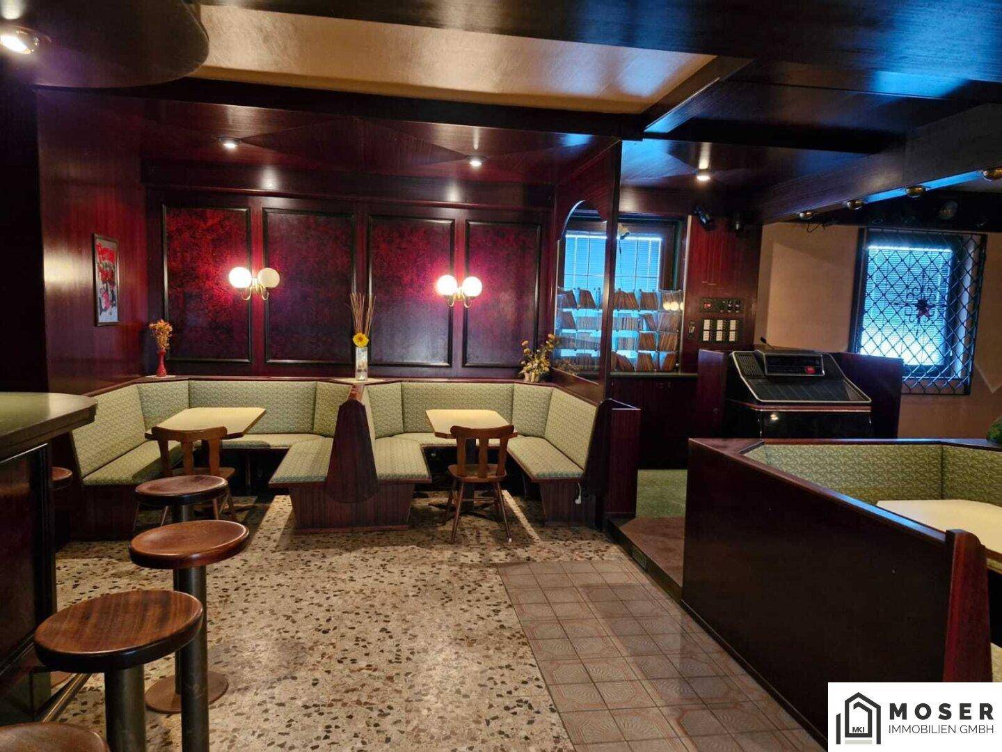 Bar-Bereich mit Hockern und dunkler Holzvertäfelung, im Hintergrund gemütliche Sitznischen.
