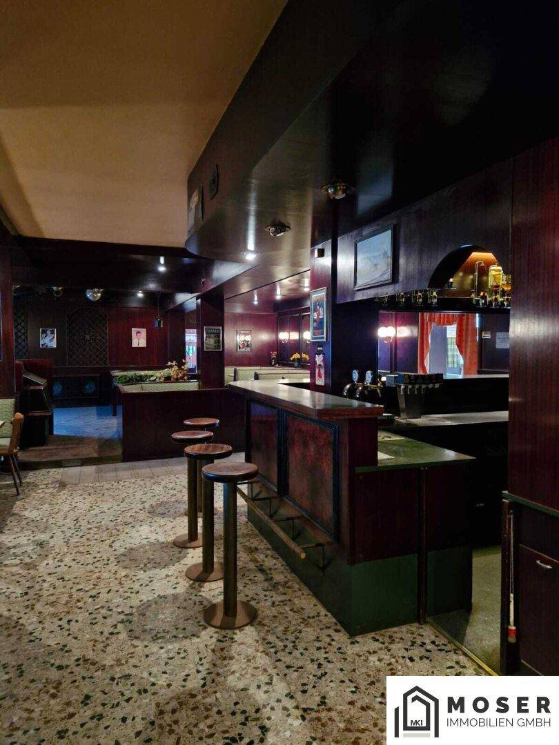 Detailansicht der Bar mit Theke, Hockern und dunkler Holzverkleidung, einladend für Gäste.