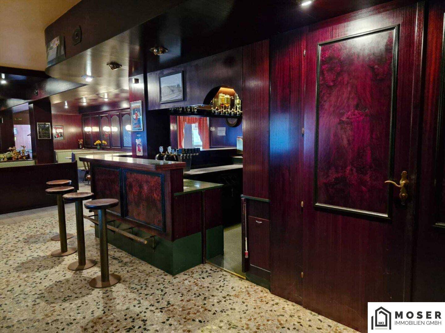 Dunkel holzvertäfelte Bar mit Theke und Hockern, ideal für gesellige Abende.