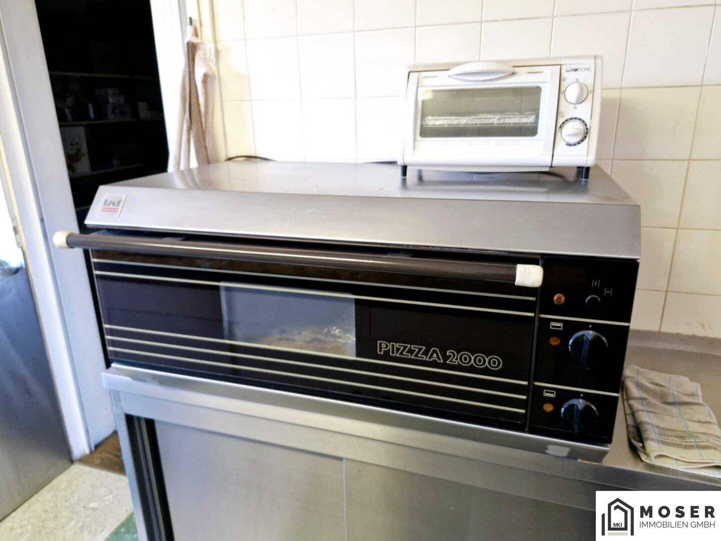 Professioneller Pizzaofen und Mikrowelle auf einer Edelstahlarbeitsfläche in der Küche.