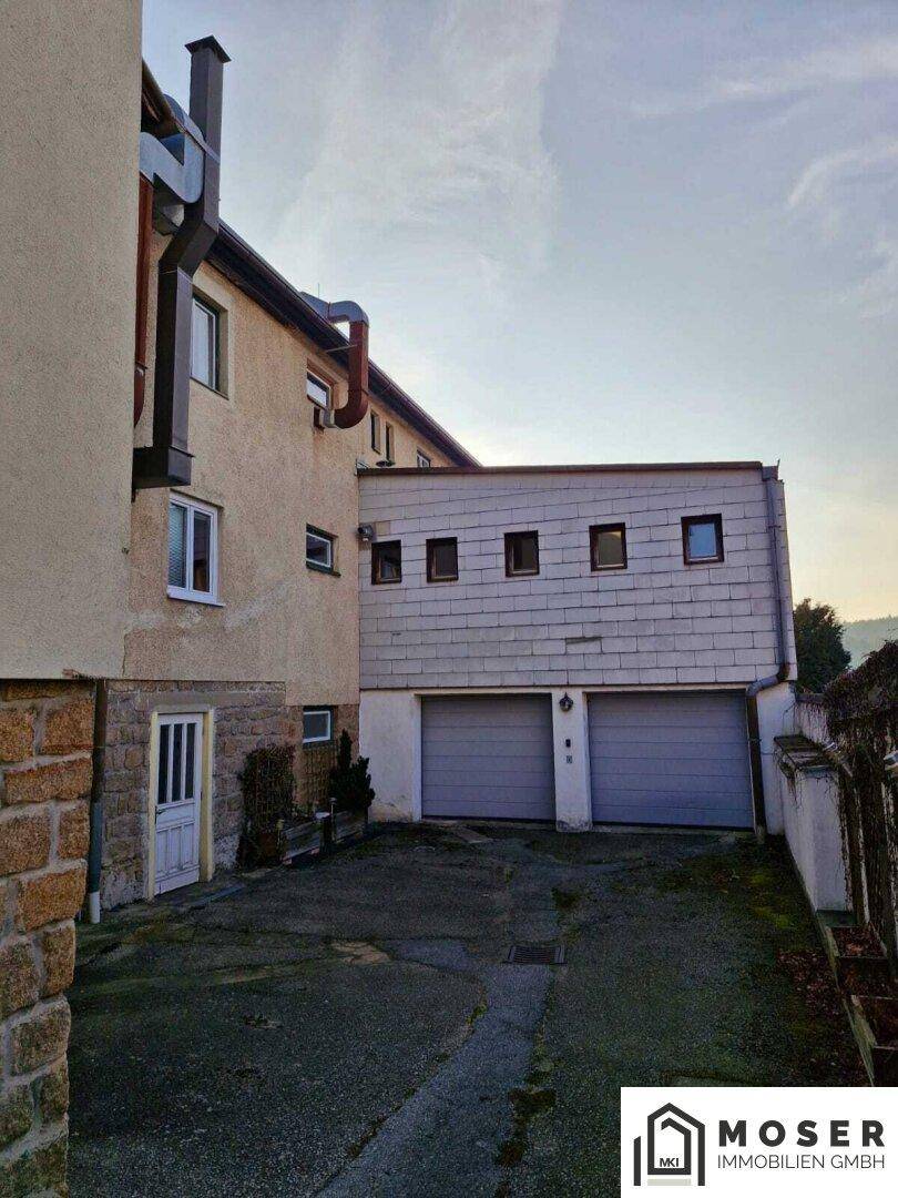 Seitenansicht des Gebäudes mit zwei Garagentoren und einem gepflasterten Zufahrtsbereich.