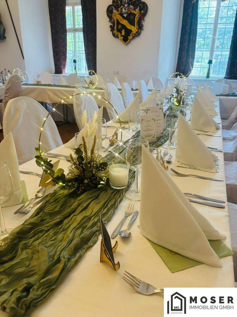 Nahaufnahme einer elegant gedeckten Tafel mit grüner Tischdeko, Kerzen und festlichem Geschirr.