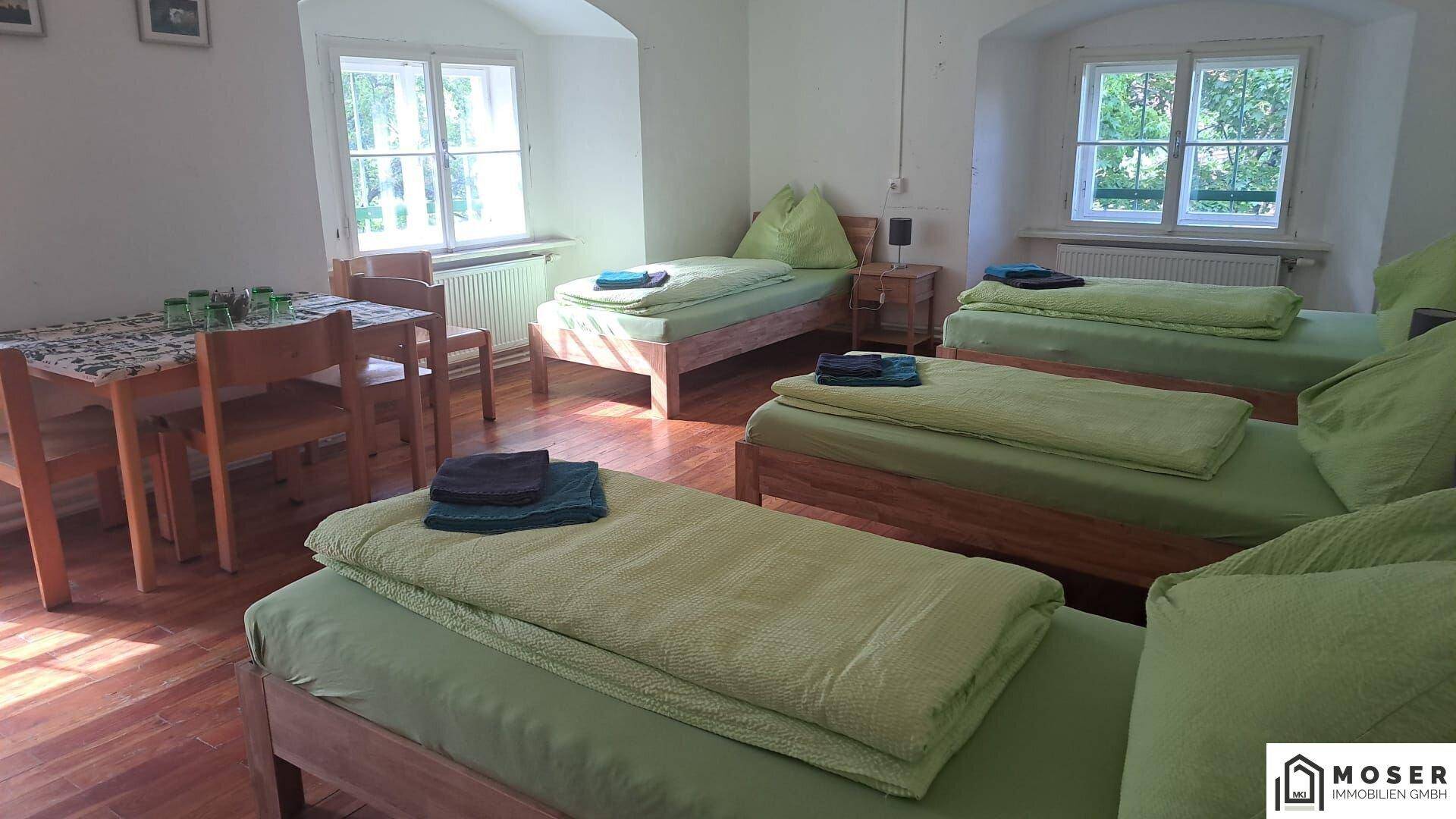 Helles Schlafzimmer mit mehreren Einzelbetten, Holzböden und einem kleinen Tisch mit Stühlen.