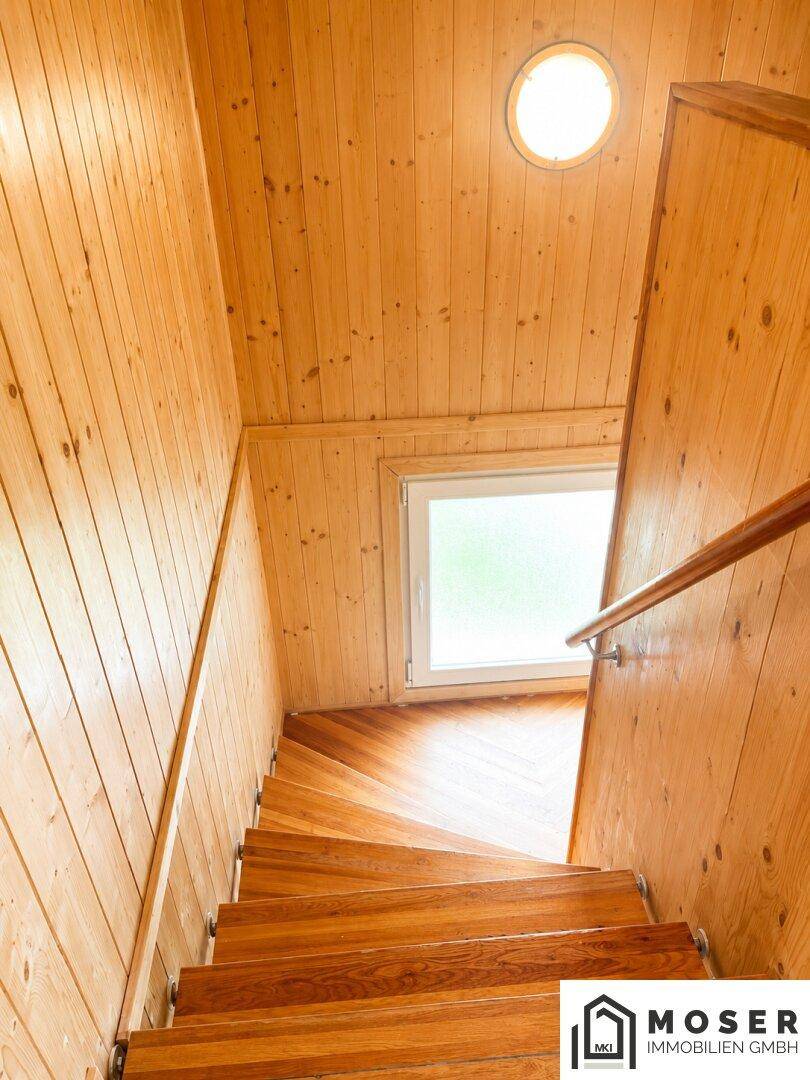 Helle Holztreppe mit Fenster und runder Deckenleuchte, die die oberen Etagen verbindet.