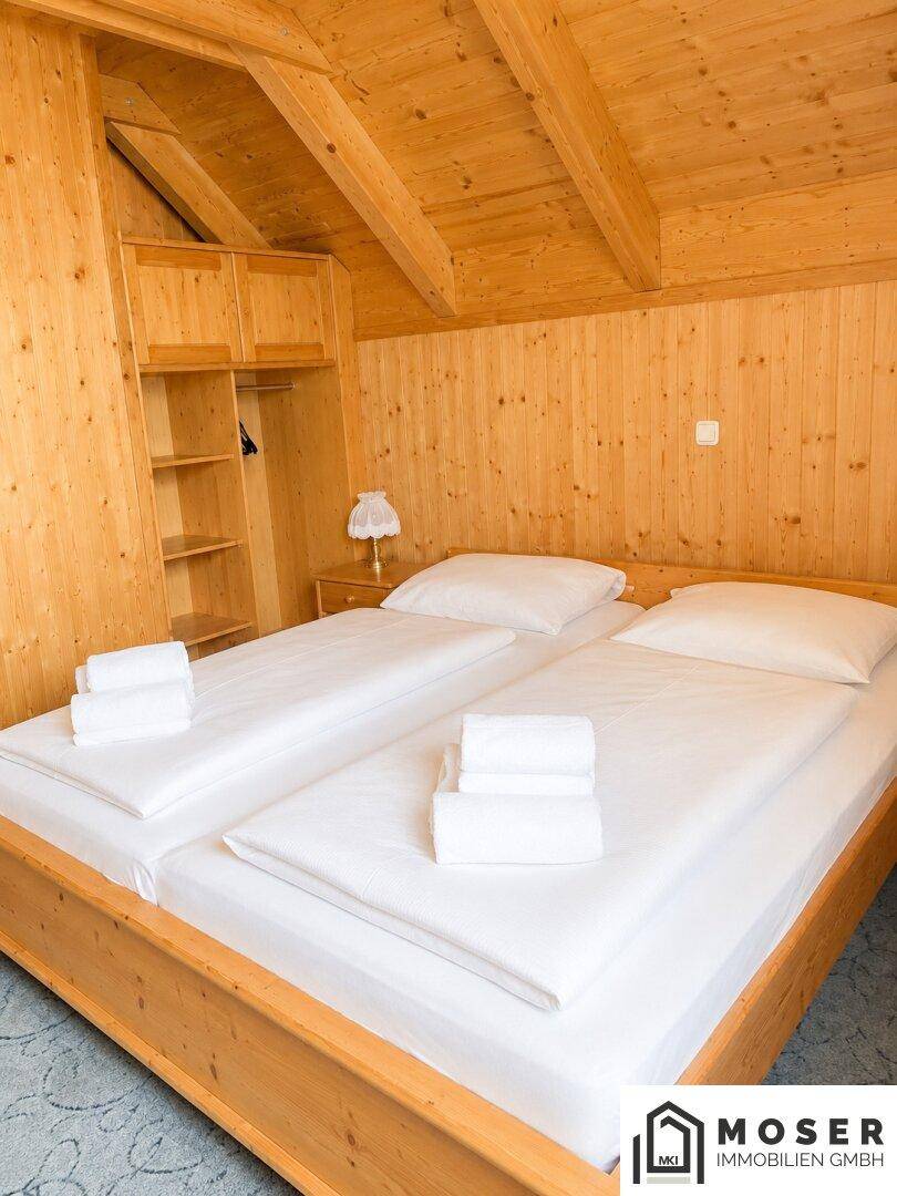 Gemütliches Schlafzimmer mit zwei Einzelbetten, Holztäfelung, Einbauschränken und Dachschräge.
