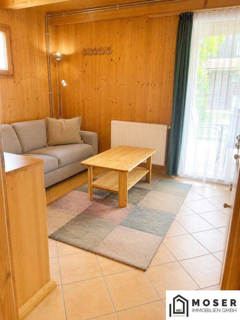 Gemütliches Wohnzimmer mit Sofa, Holztäfelung, Fliesenboden und Zugang zu einem Außenbereich.