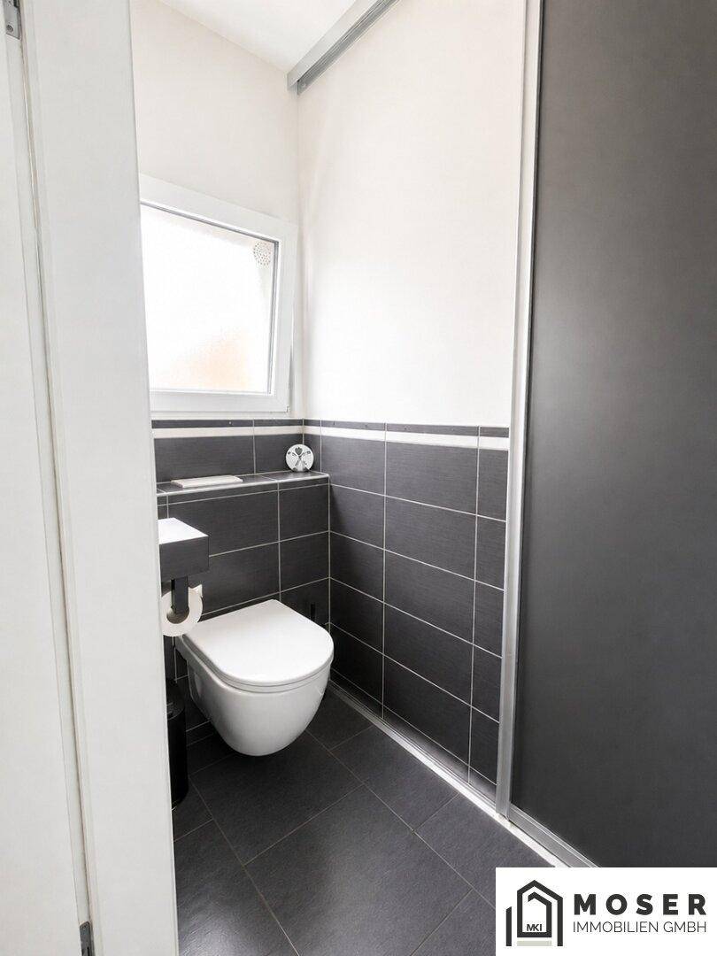 Modernes Gäste-WC mit dunklen Fliesen, wandhängendem WC und Fenster.
