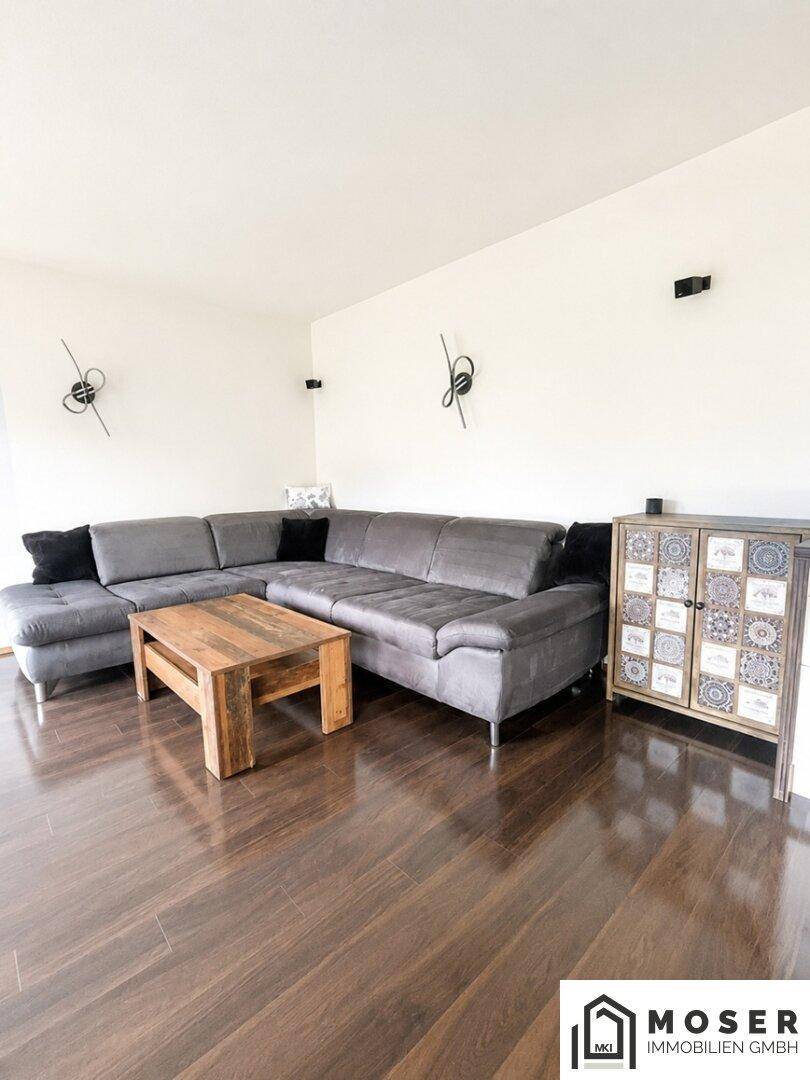 Gemütliches Wohnzimmer mit großem Ecksofa, Holztisch und dunklem Parkettboden.