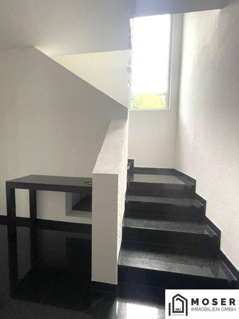 Elegante Treppe mit dunklen Granitstufen und hellem Geländer, gut beleuchtet durch ein Fenster.