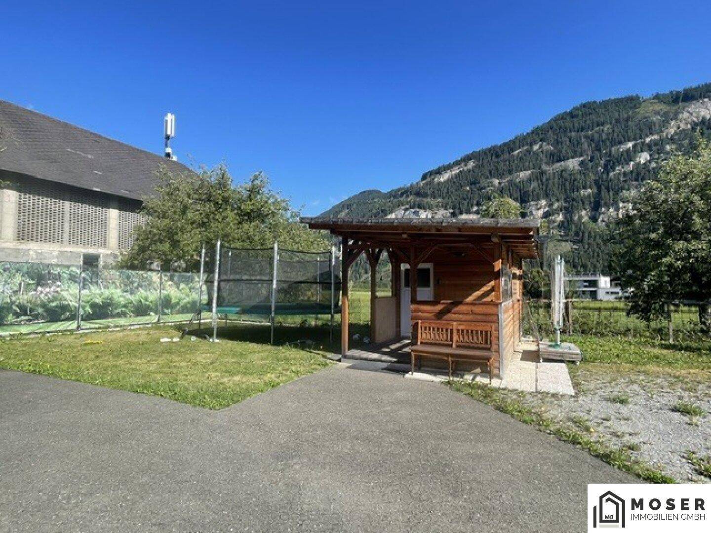 Kleines Holzhaus im Gartenbereich mit Trampolin und Blick auf die grüne Berglandschaft.