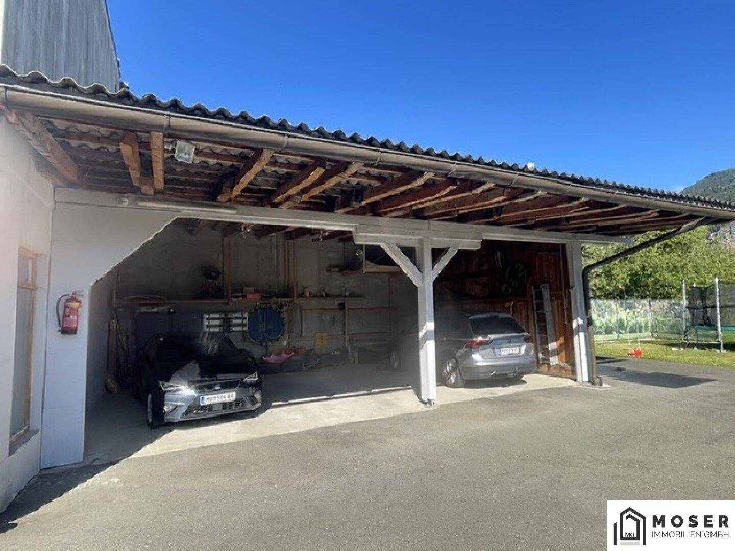 Überdachter Carport mit zwei geparkten Autos und Blick auf die umliegende Berglandschaft.