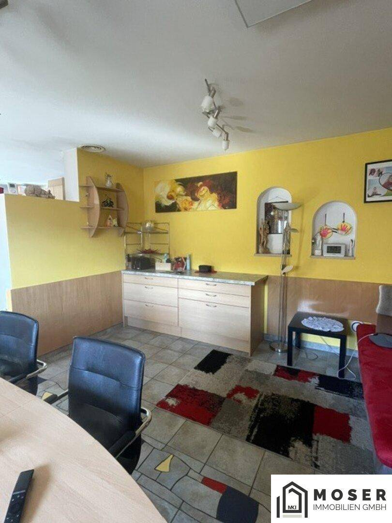 Wohnbereich mit gelben Wänden, Sideboard und Teppich, angrenzend an den Essbereich.