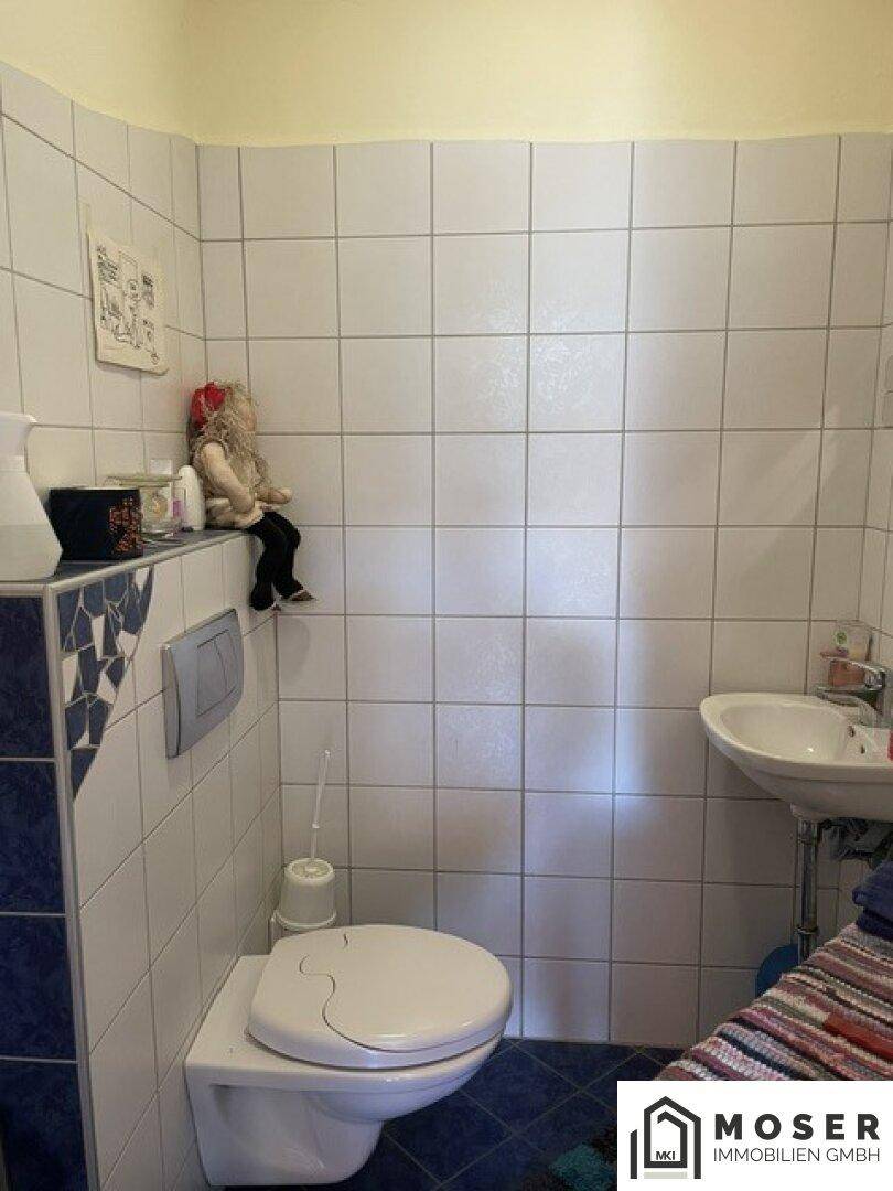 Einfaches Gäste-WC mit weißen Fliesen, Wand-WC und kleinem Waschbecken.