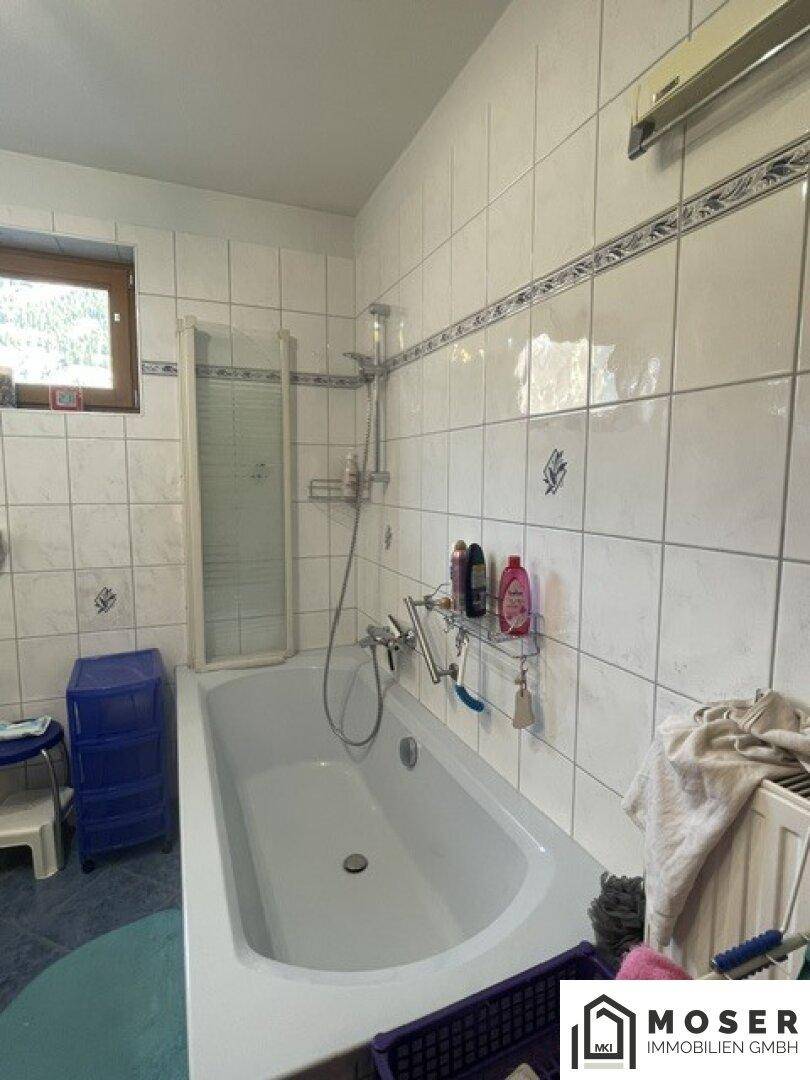 Helles Badezimmer mit Badewanne, Duschvorrichtung und Fenster, komplett gefliest.