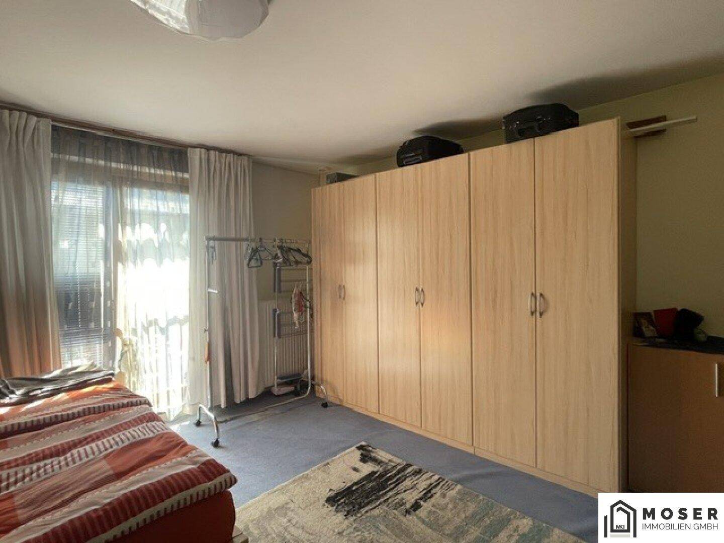 Schlafzimmer mit großem Einbauschrank, Fenster mit Vorhängen und Teppichboden.