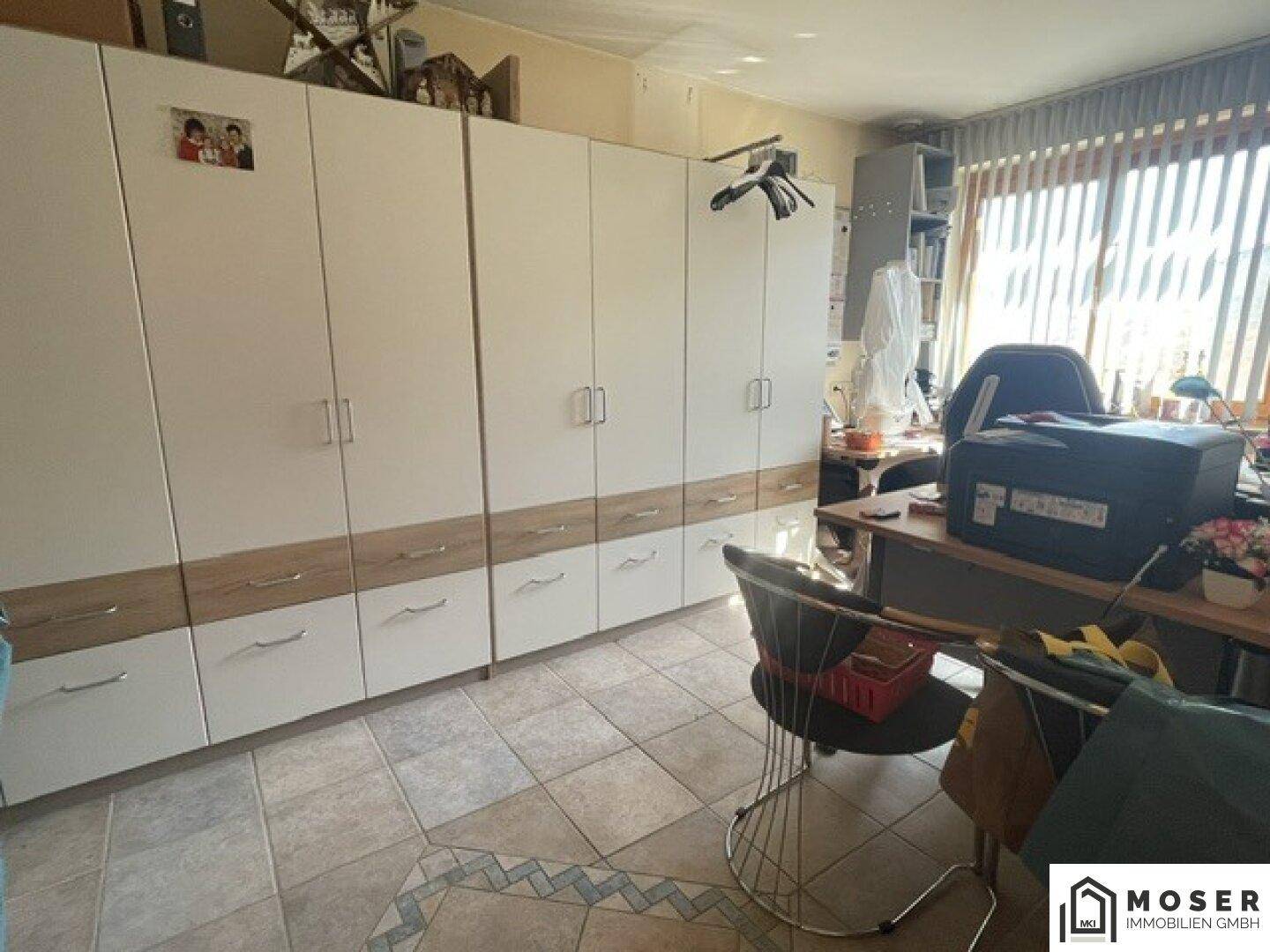 Raum mit großem Einbauschrank, Schreibtisch und Fliesenboden, ideal als Arbeitszimmer nutzbar.