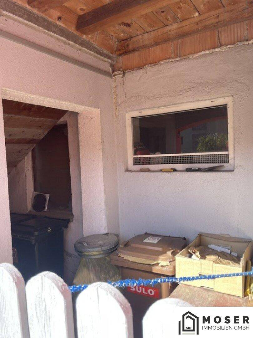 Einfacher Eingangsbereich oder Abstellraum mit kleinem Fenster und sichtbaren Holzbalken.