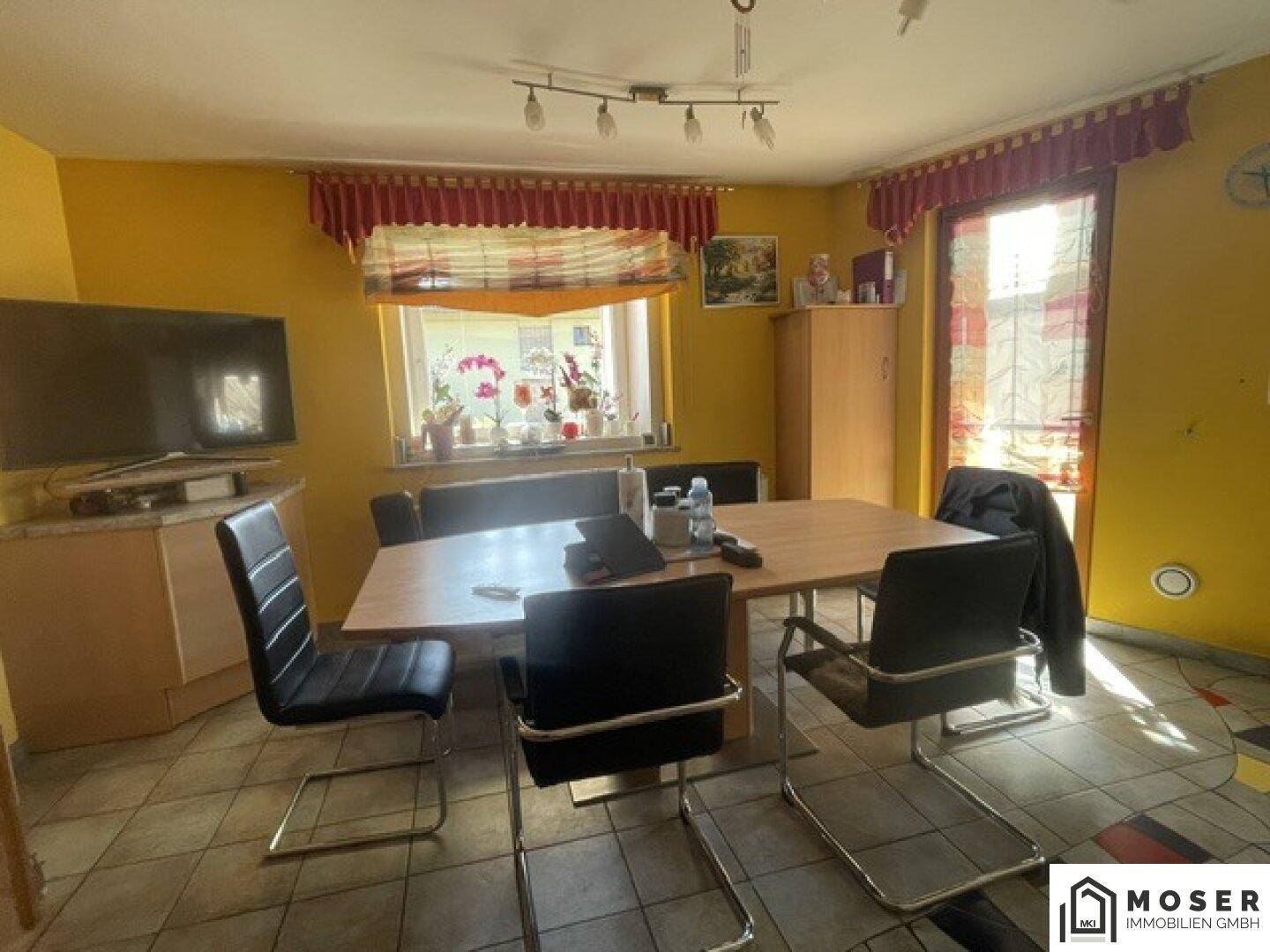 Gemütlicher Essbereich mit Holztisch und Stühlen, umgeben von gelben Wänden und Fliesenboden.