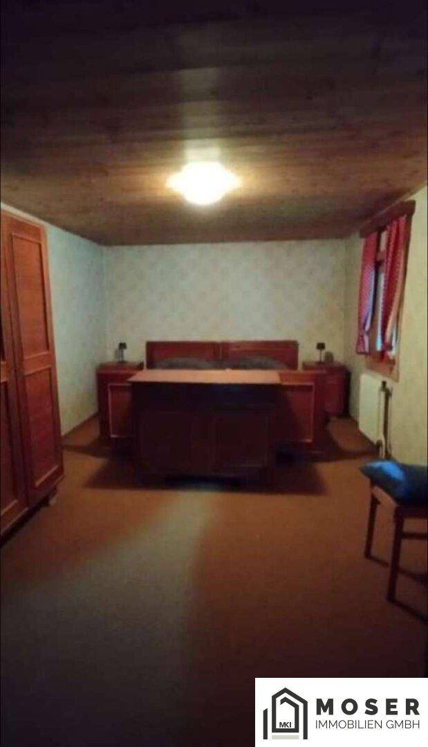 Schlafzimmer mit traditionellen Holzmöbeln und einer Holzbalkendecke.