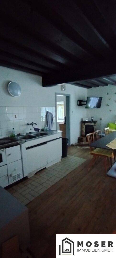 Einfache Küche mit weißen Schränken, gefliestem Spritzschutz und Holzboden.