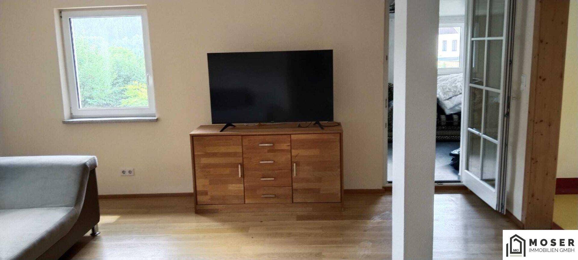 Wohnzimmer mit Fernseher auf Holzkommode und hellem Holzparkettboden.