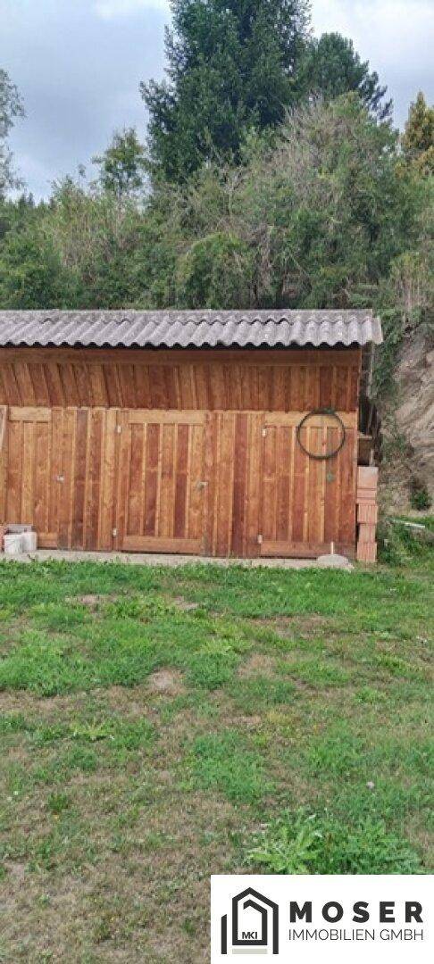 Rustikaler Holzschuppen im Gartenbereich mit Wellblechdach.