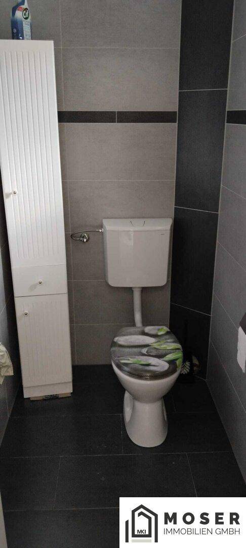 Separate Toilette mit modernen grauen Fliesen und weißem Schrank.
