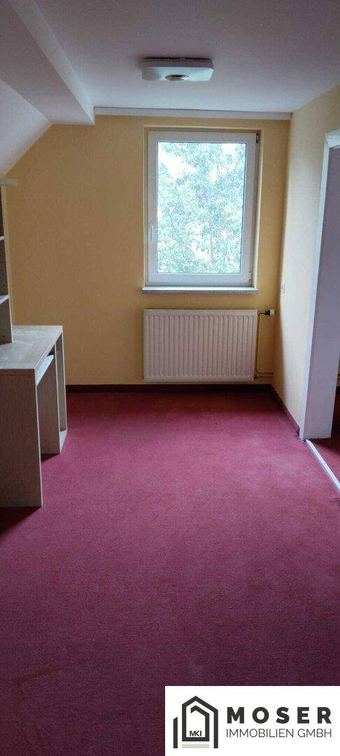Helles Schlafzimmer mit rotem Teppichboden und Fenster mit Blick ins Grüne.