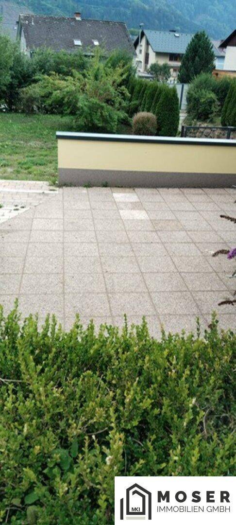 Gepflasterte Terrasse mit niedriger Mauer und Blick auf die Nachbarschaft.
