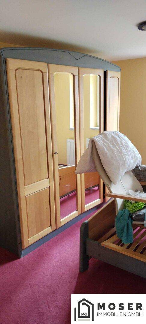 Schlafzimmer mit großem Holzschrank, Spiegeltüren und rotem Teppichboden.