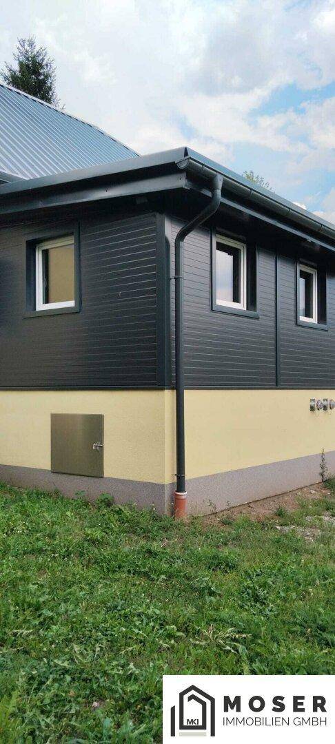 Moderner Anbau des Hauses mit dunkler Holzverkleidung und gelbem Sockel.