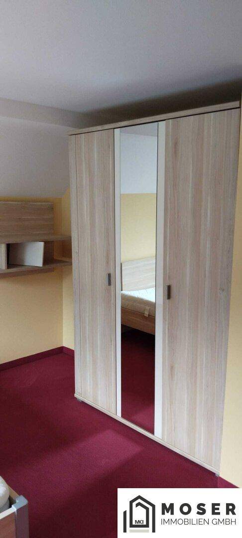 Schlafzimmer mit hellem Holzschrank, Spiegeltüren und rotem Teppichboden.