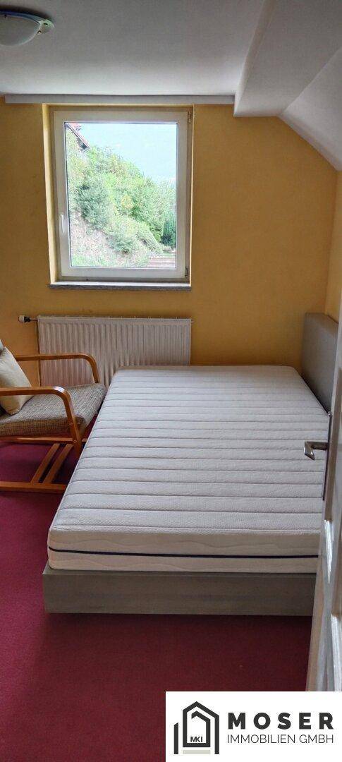 Helles Schlafzimmer mit Einzelbett, rotem Teppichboden und Fenster.