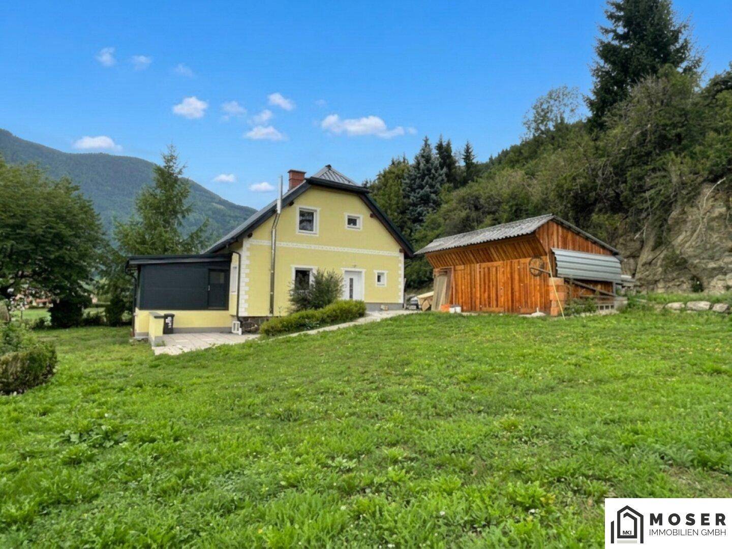 Großzügiger Gartenbereich mit gelbem Haus, Holzschuppen und Bergblick.