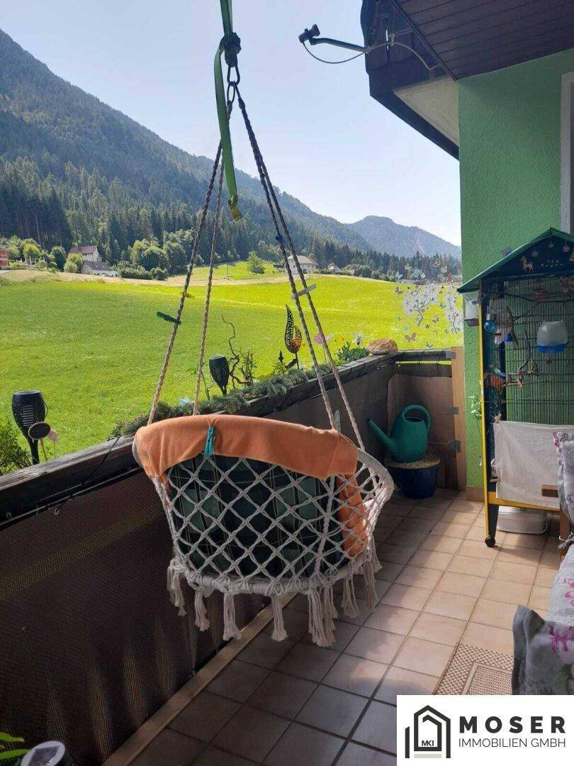 Gemütlicher Balkon mit Hängesessel und weitem Blick auf die grüne Berglandschaft und umliegende Häuser.