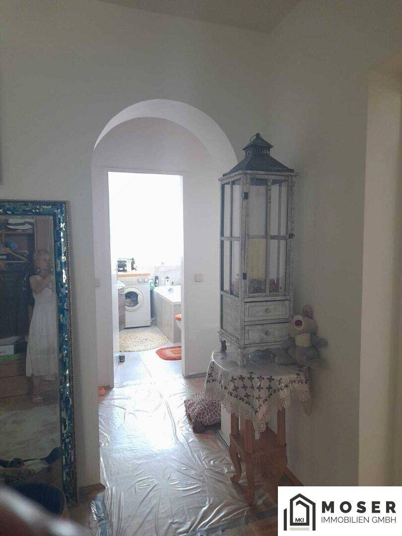 Heller Flur mit einem dekorativen Schrank und Blick in ein Badezimmer mit Waschmaschine.