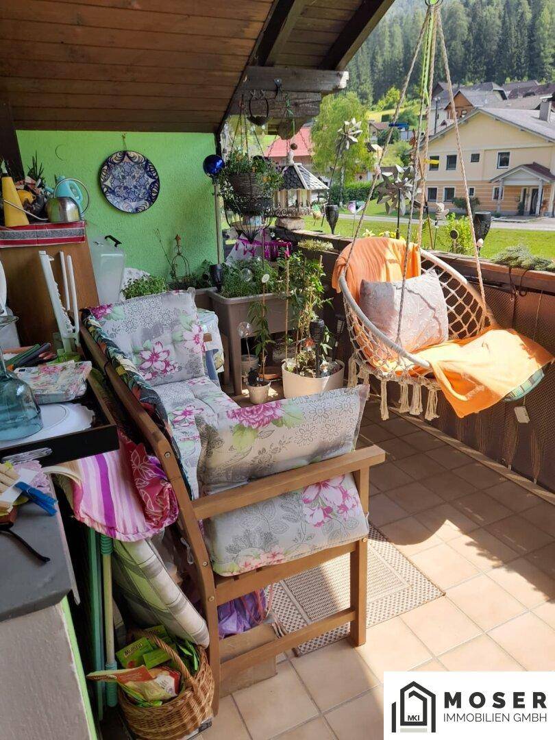 Möblierter Balkon mit Pflanzen, Hängesessel und Blick auf die umliegende Landschaft und Häuser.