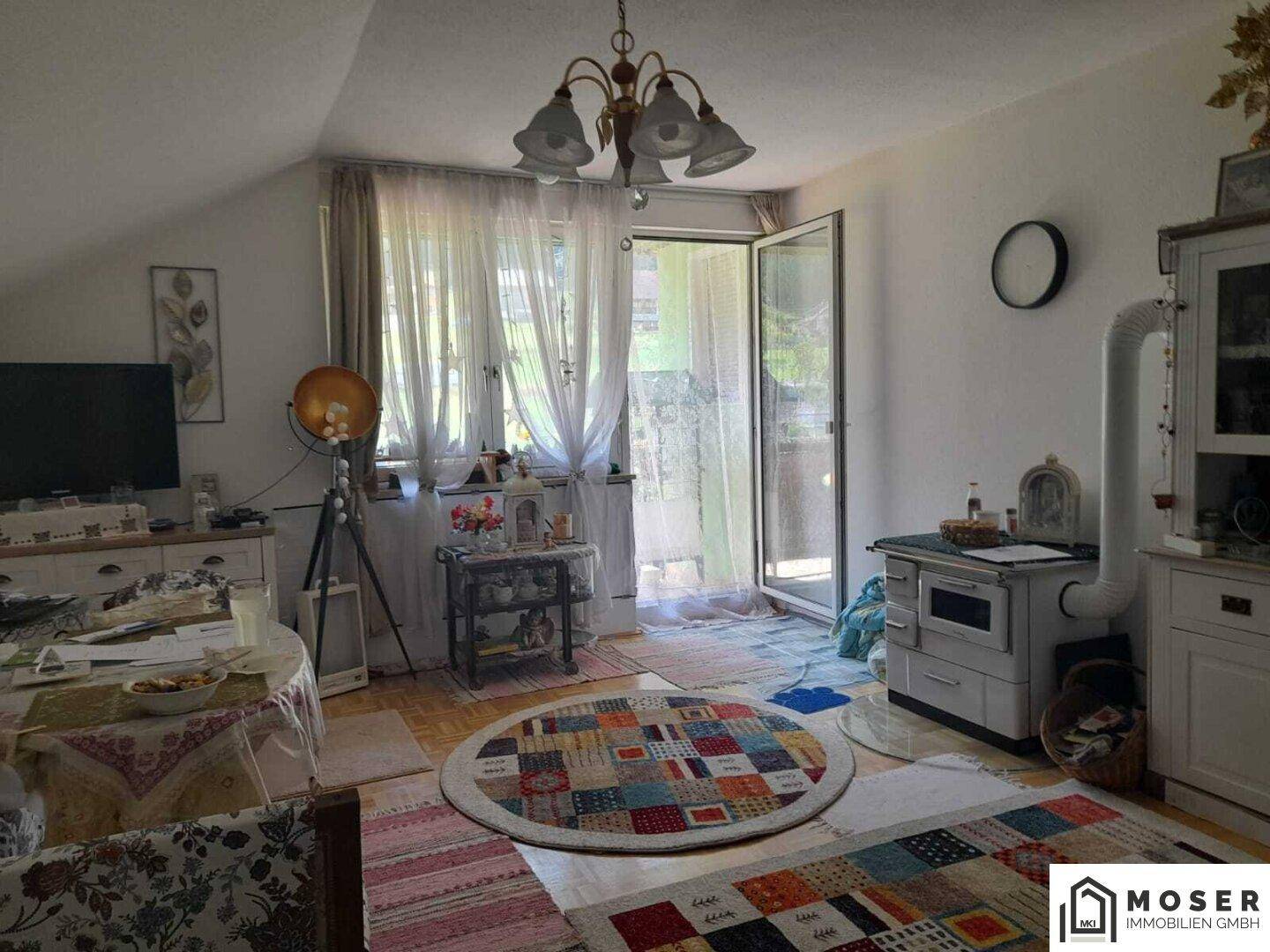 Rustikales Wohnzimmer mit Holzboden, Kachelofen und Zugang zu einem Balkon unter einer Dachschräge.