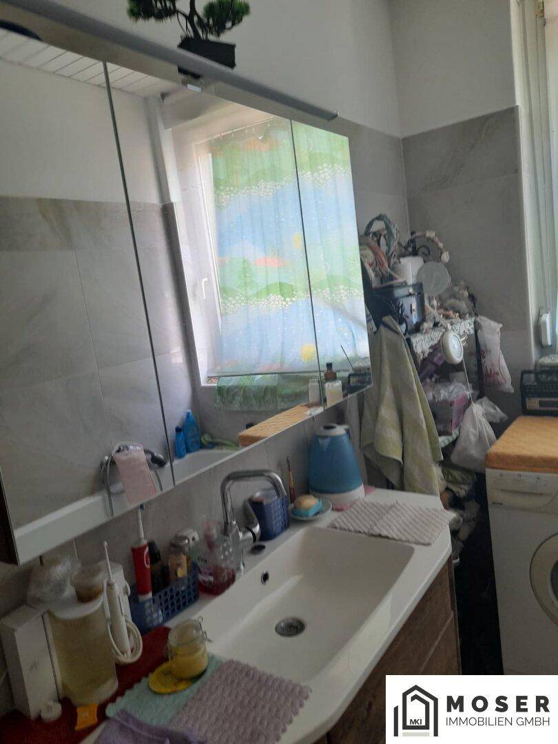 Badezimmer mit Waschbecken, Spiegelschrank und Fenster, das viel Tageslicht hereinlässt.